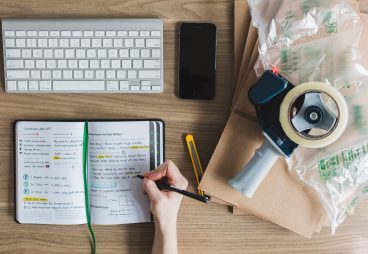 persoon aan het werk met toetsenbord, telefoon en aantekeningen